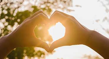 Image of hands forming a heart shape with sun behind them